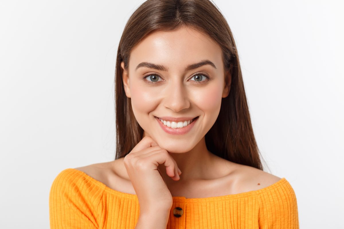 Smiling woman in yellow shirt posing against white background for orthodontics website portrait.