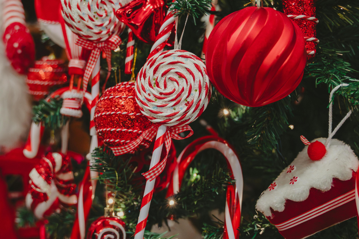 Holiday Treats Your Teeth Secretly Fear Christmas Foods That Harm Teeth Red and white Christmas ornaments and candy decorations on evergreen tree branches.