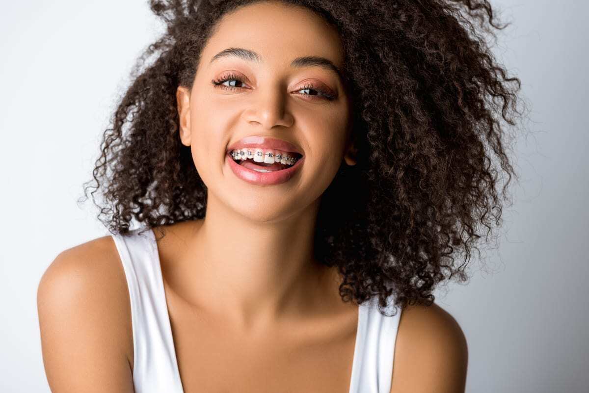 Orthodontics in Pearl Young woman with curly dark hair smiling brightly, displaying healthy teeth after orthodontic treatment.